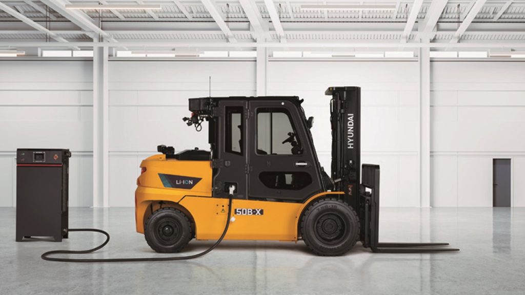 Hyundai 50B-X lithium-ion electric forklift connected to a charging unit inside a warehouse