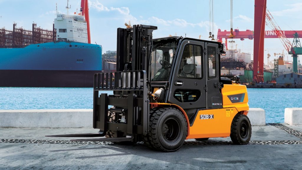 Hyundai 50B-X high-voltage electric forklift parked at a port with container ships and cranes in the background