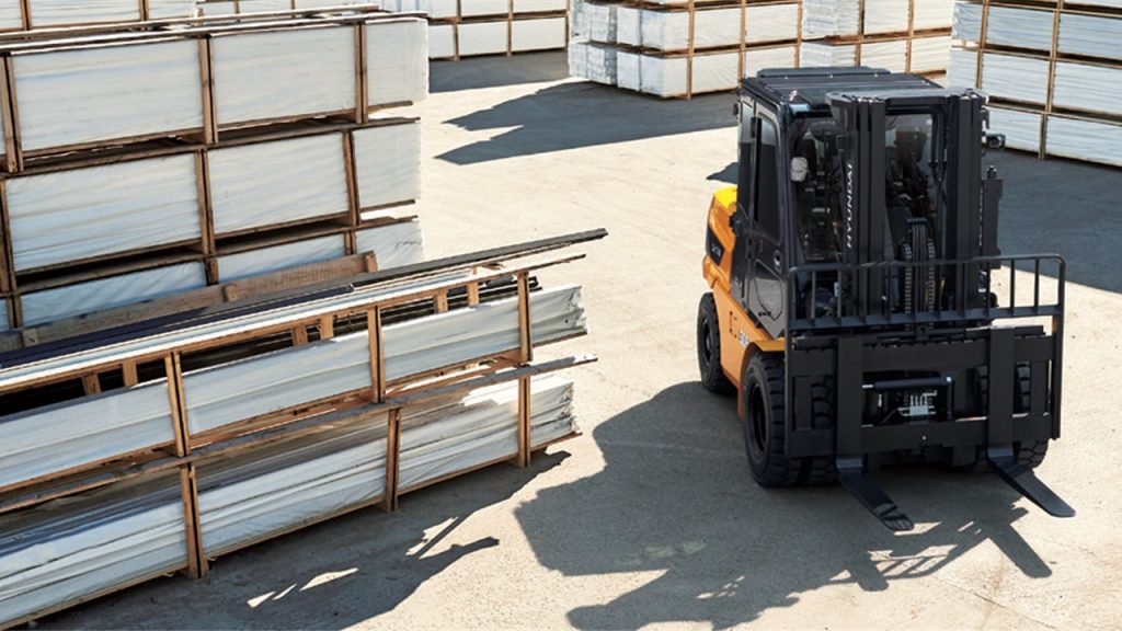 Hyundai B-X Series electric forklift handling stacked sheet material at an outdoor industrial yard